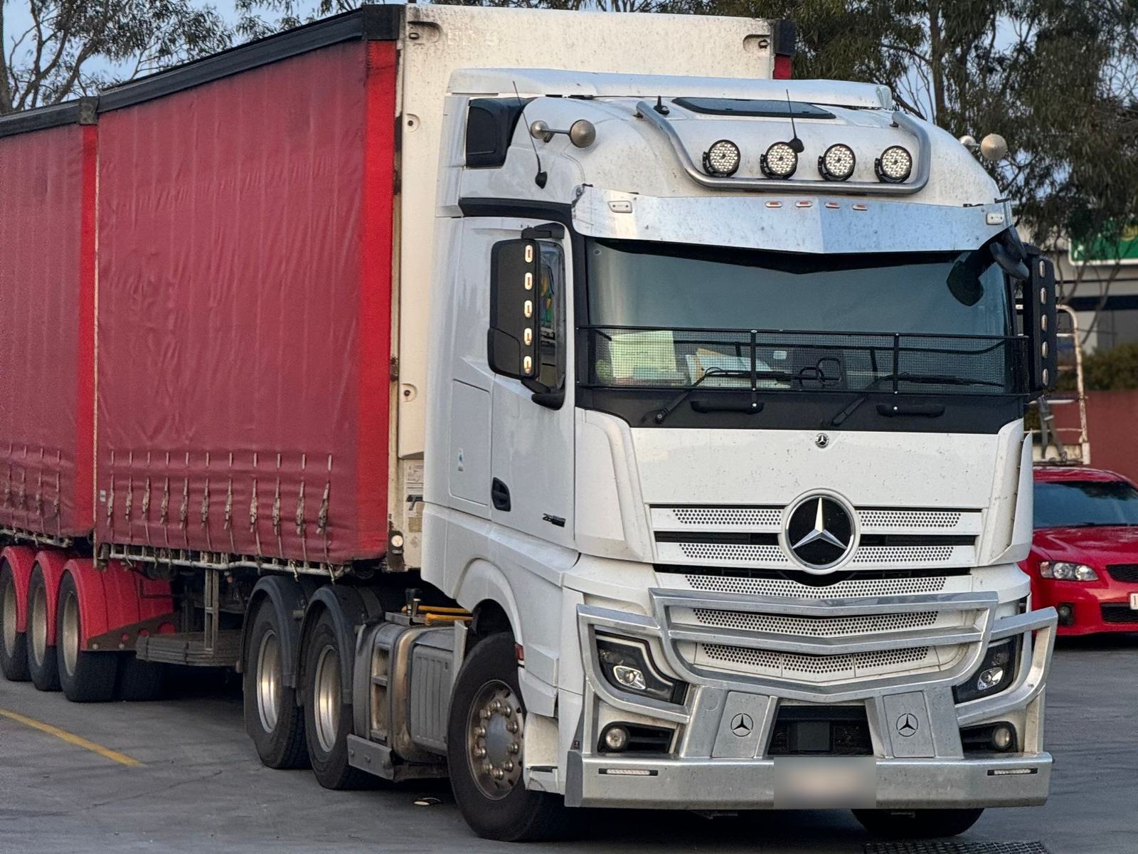 Tracteur blanc et semi-remorque rouge à bâche, prêts au départ